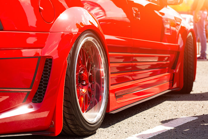 A close-up of a red custom car with chrome rims, shining in the sun, showing karma's instant justice.