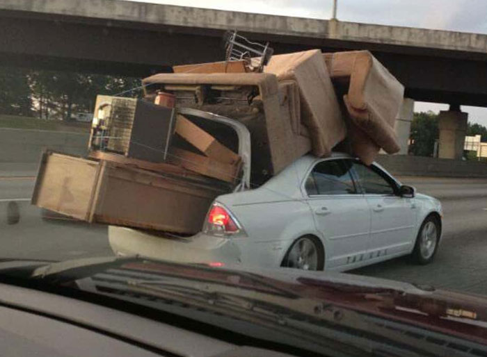 Sedan overloaded with furniture on roof and trunk depicts moving fails