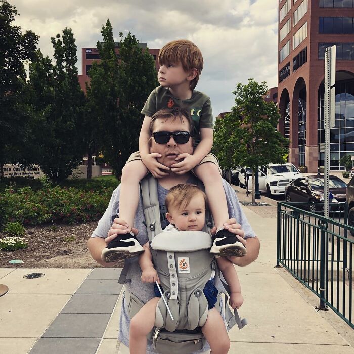 A man carrying two children, one on his shoulders and one in a baby carrier, proof they found the right man.