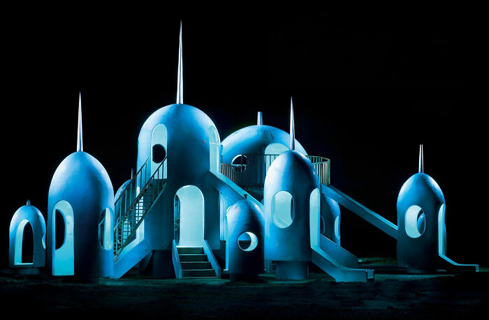 A blue rocket-themed playground structure at night, from the surreal Japanese playgrounds by Fujio Kito.