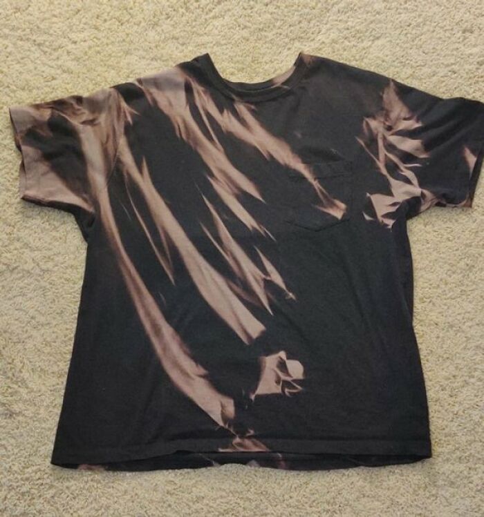 A black t-shirt with a cool bleach pattern showing what happens if you accidentally splash bleach on it.