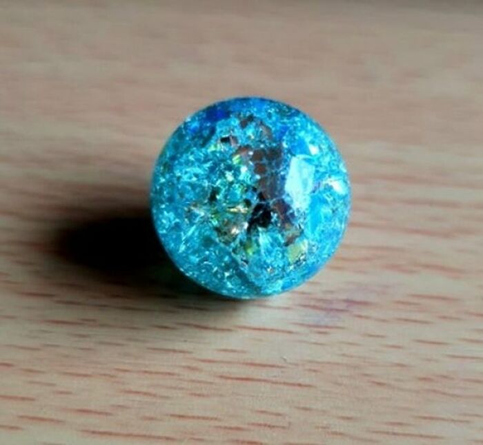 A vibrant blue cracked glass marble sitting on a wooden surface, displaying cool photos of everyday objects