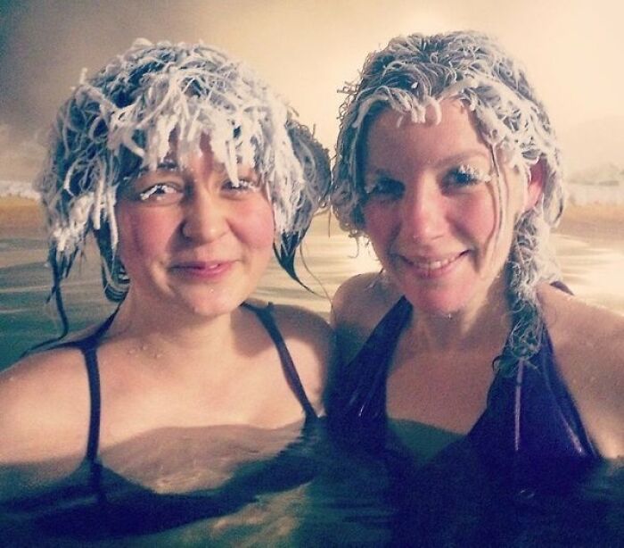 Two women smiling in a hot spring with frozen hair, showcasing cool photos of unusual winter phenomena