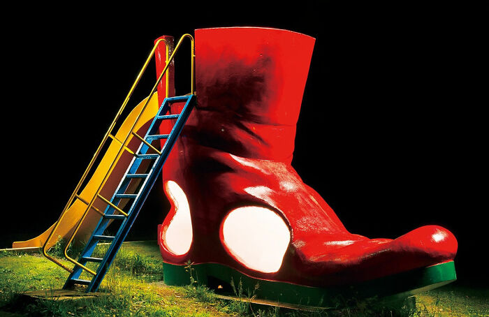 A giant red boot playground slide at night, one of the surreal Japanese playgrounds by Fujio Kito.
