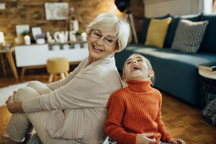 Happy grandmother sitting back-to-back with her laughing granddaughter, illustrating a family bond. Happy grandmother sitting back-to-back with her laughing granddaughter, illustrating a family bond.