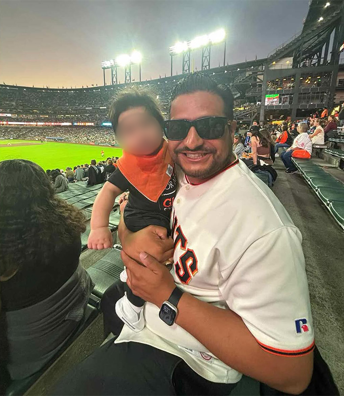Man holding child at baseball game wearing Giants jersey and sunglasses