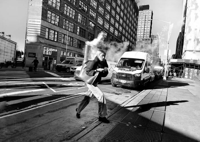 A woman runs across a city street with steam rising, capturing a fleeting moment in street photos by Taylor Coble.