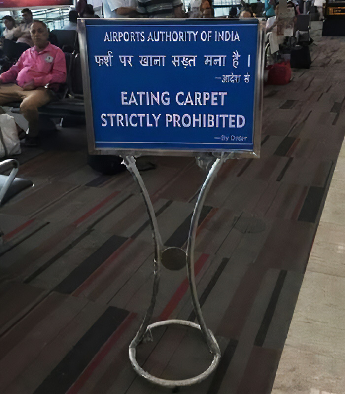 A silly sign at an airport states EATING CARPET STRICTLY PROHIBITED. This funny sign is placed in the middle of a busy airport terminal.