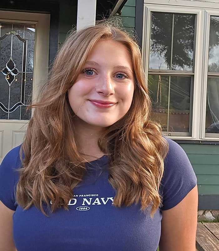 A smiling honors student with long, wavy hair, involved in a school coffee rule challenge.