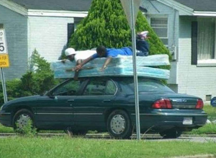Car carrying mattress with person lying on top illustrates moving fails
