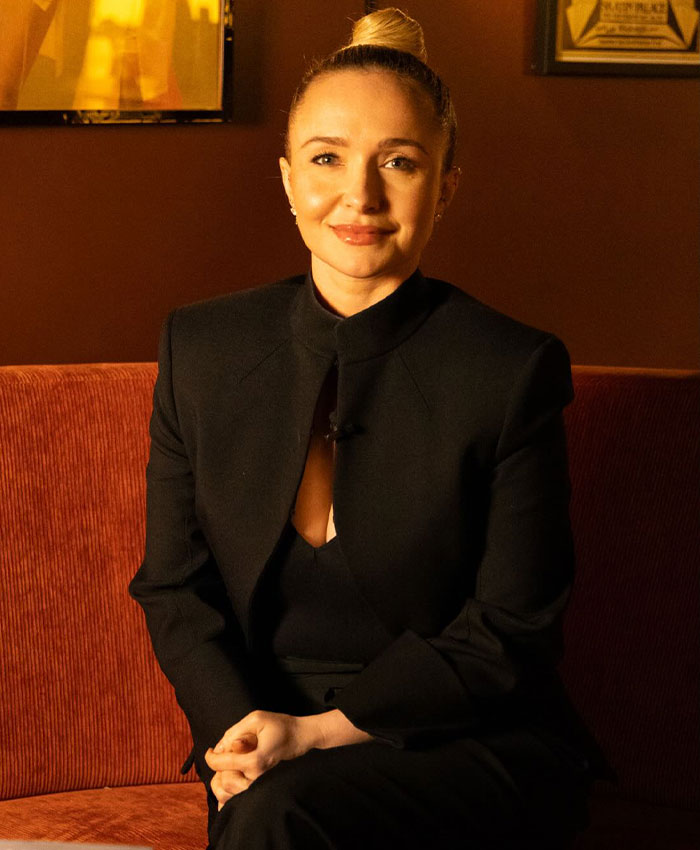 Hayden Panettiere in a black suit sitting on an orange couch. Hayden Panettiere in a black suit sitting on an orange couch.