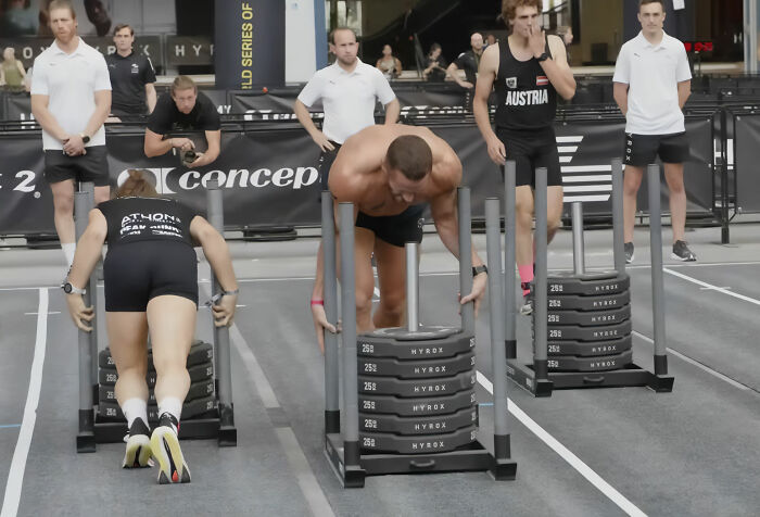 HYROX athletes push sleds during a race, facing intense backlash after an athlete soiled herself but refused to quit.