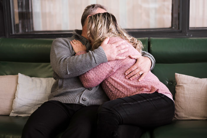 A man comforting a woman crying on a green sofa, illustrating severe pain following surgery