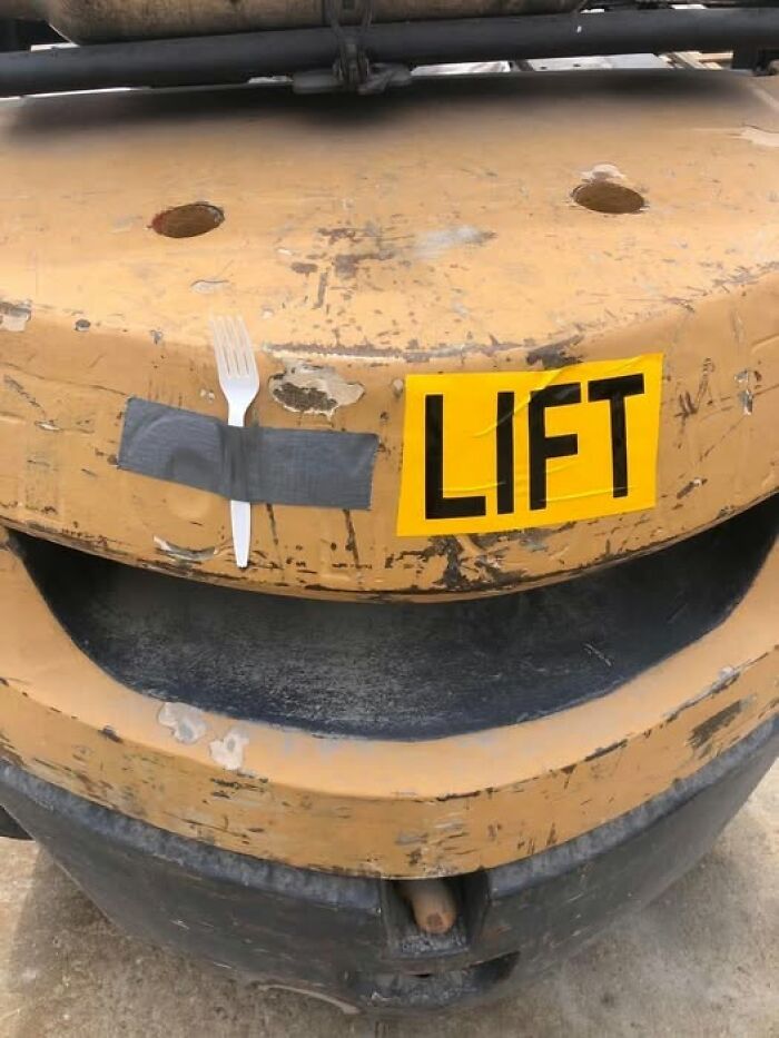 A silly funny sign with a fork taped next to a LIFT sticker on a piece of heavy machinery.