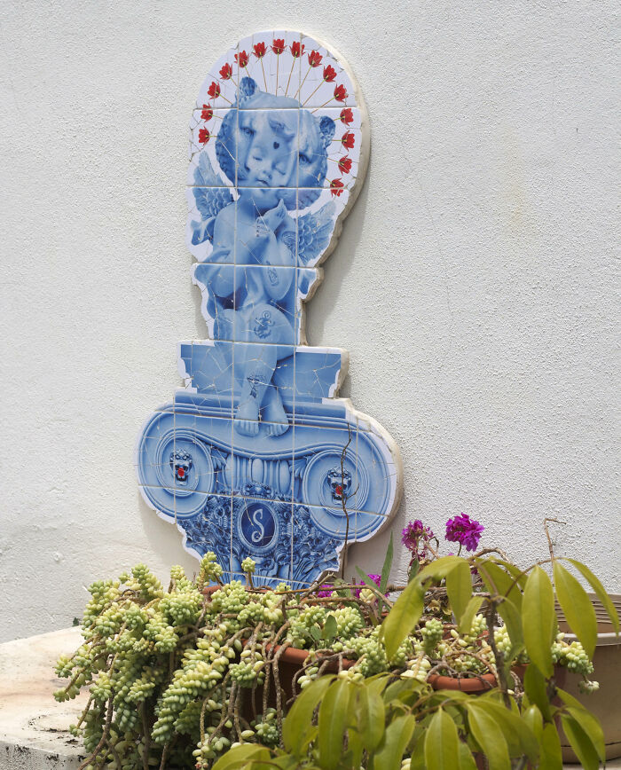 Blue tile works of an angelic cherub statue with red flower halo on white wall