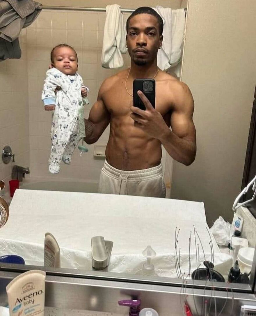 A chaotic and disturbing pic of a man holding a baby in front of a mirror, making you doubt sanity.