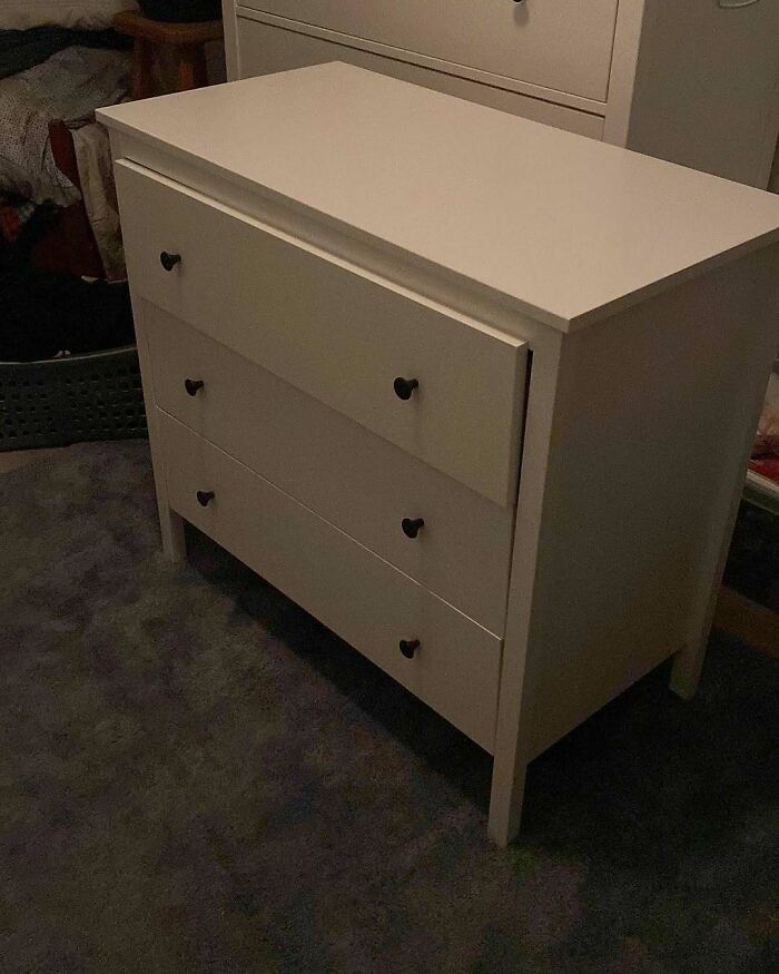 A poorly assembled white chest of drawers with a drawer open, exemplifying questionable home improvement results.