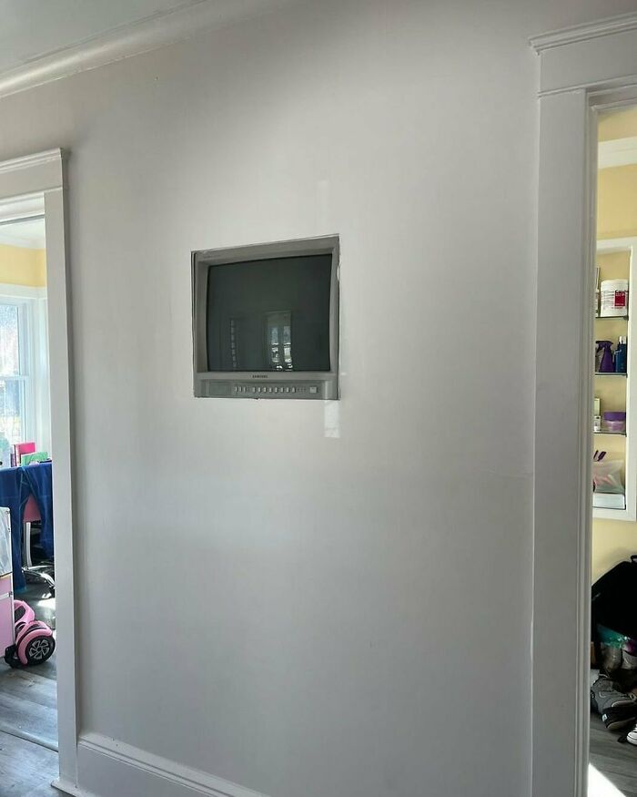 A questionable home improvement project with a small, old TV unprofessionally recessed into a plain white wall.