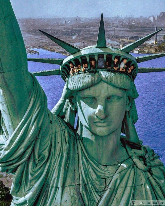 Historical colorized photo of people looking out from the crown of the Statue of Liberty.