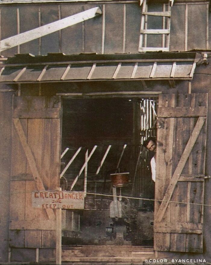 Historical colorized photo of a man peeking from a barn door with a danger sign, making the past days come to life.