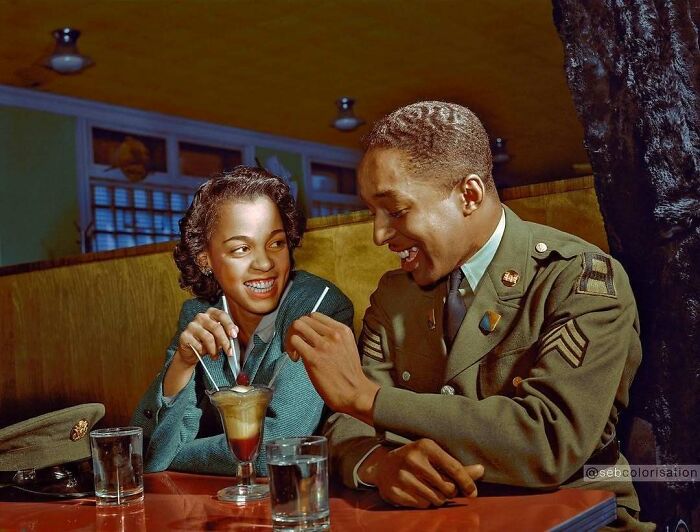 Historical colorized photo of a smiling couple, a woman and a man in a military uniform, enjoying drinks.
