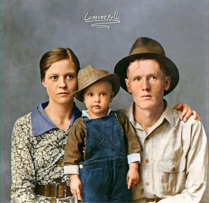 Historical colorized photo of a solemn family with a young child in overalls and a hat.