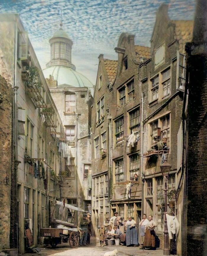 Historical colorized photo of a narrow European street with people and clotheslines, making the past days come to life.