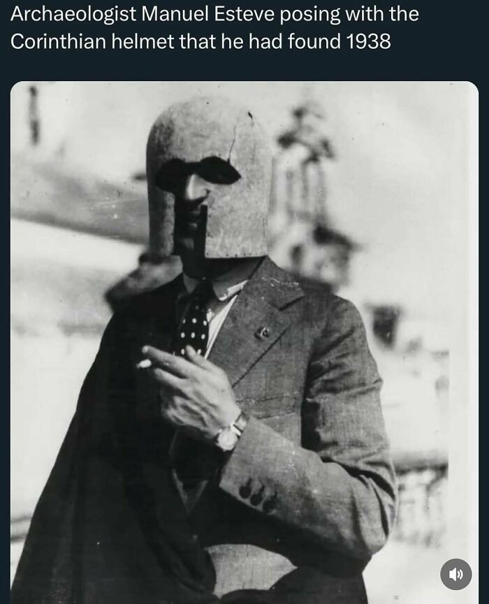 Black and white photo of archaeologist posing with ancient Corinthian helmet