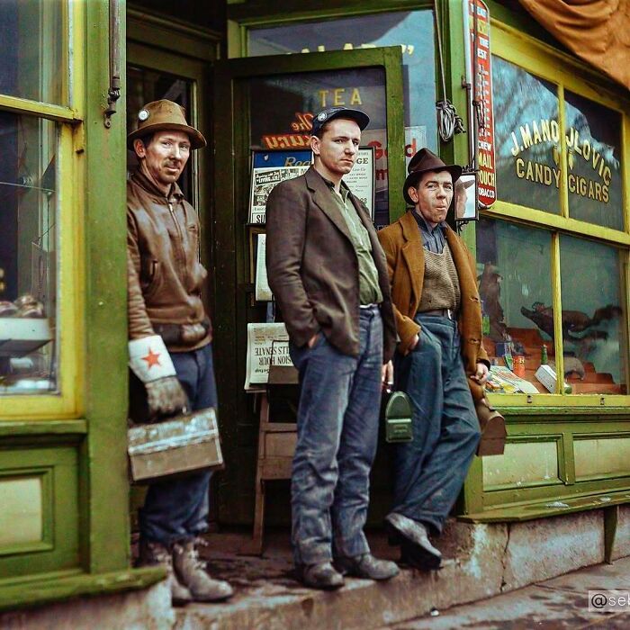 Three men, possibly miners, stand outside a shop in a street scene from a stunning historical colorized photo.