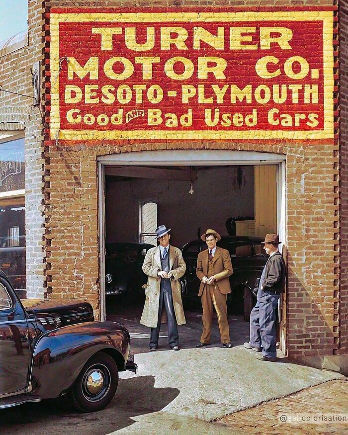 A historical colorized photo of three men standing outside a car garage under a large sign. Stunning historical colorized photos.