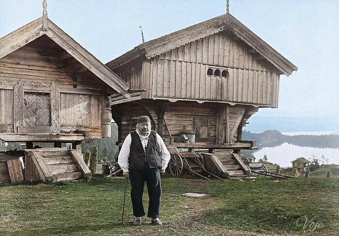 A historical colorized photo of a man standing in front of traditional wooden buildings, showcasing past days.