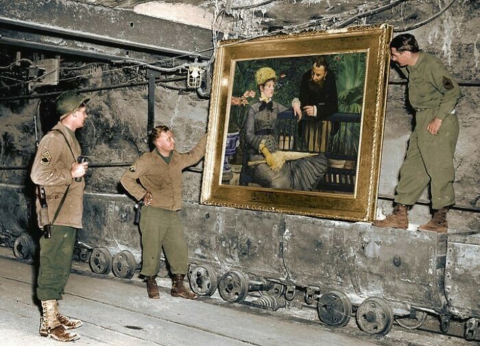 Three soldiers inspect a large historical colorized painting in a dimly lit underground bunker.