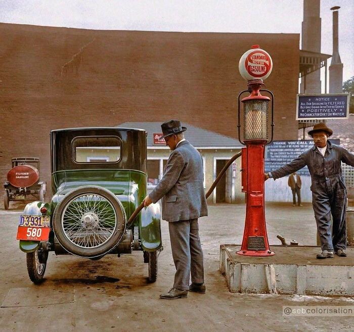 Two men at a gas pump, one fueling an antique car. Stunning historical colorized photos.