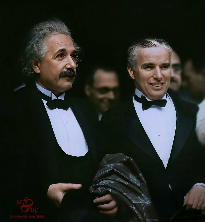 Historical colorized photo of Albert Einstein and Charlie Chaplin in tuxedos, smiling.