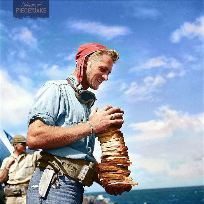 A historical colorized photo of a man in a red hat holding a stack of sandwiches, smiling. Stunning historical colorized photos.