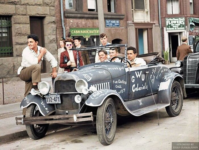 Young men and women gather around a vintage car with writing on it, a stunning historical colorized photo.