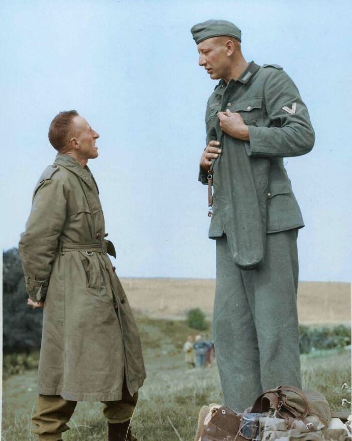 A historical colorized photo shows a tall German soldier towering over a shorter British soldier during a discussion.