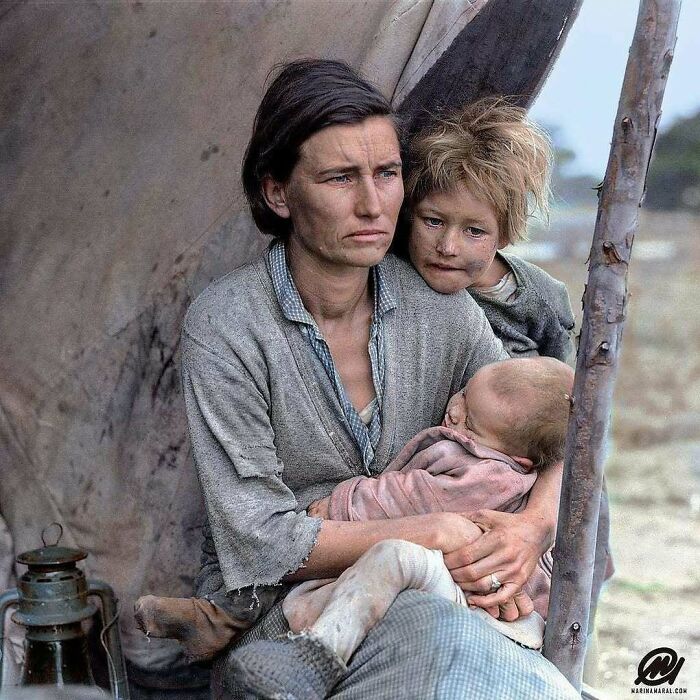A historical colorized photo of a mother holding her baby and a child peeking over her shoulder in a tent.