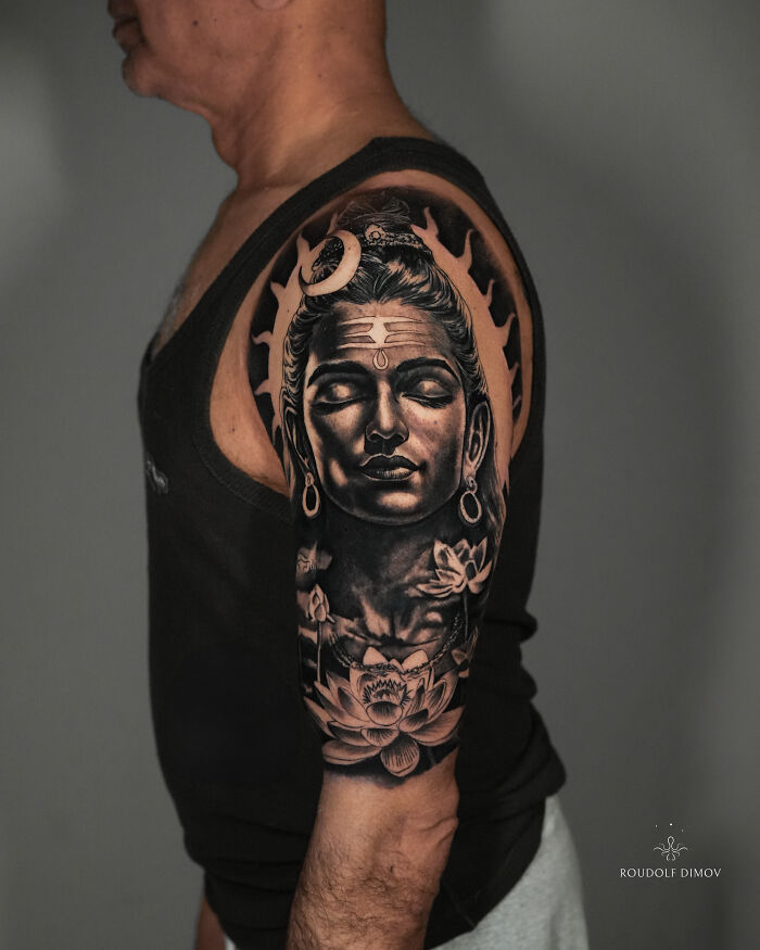 Detailed ancient mythology tattoo of a serene figure with spiritual geometry, lotus flowers, and a crescent moon, from Sacred Gold Studio.