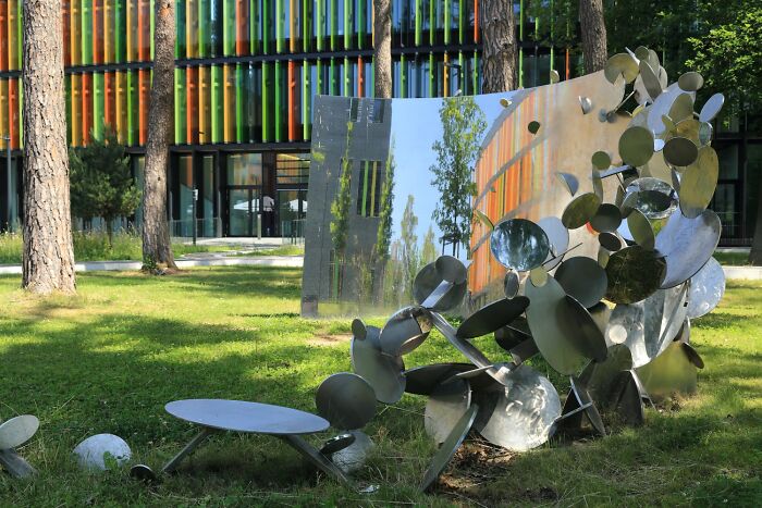Reflective sculptures made of polished metal discs in a grassy park with trees behind