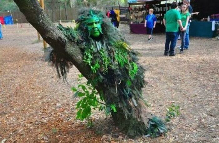 Unhinged image of a person in a green ghillie suit blending with a tree.