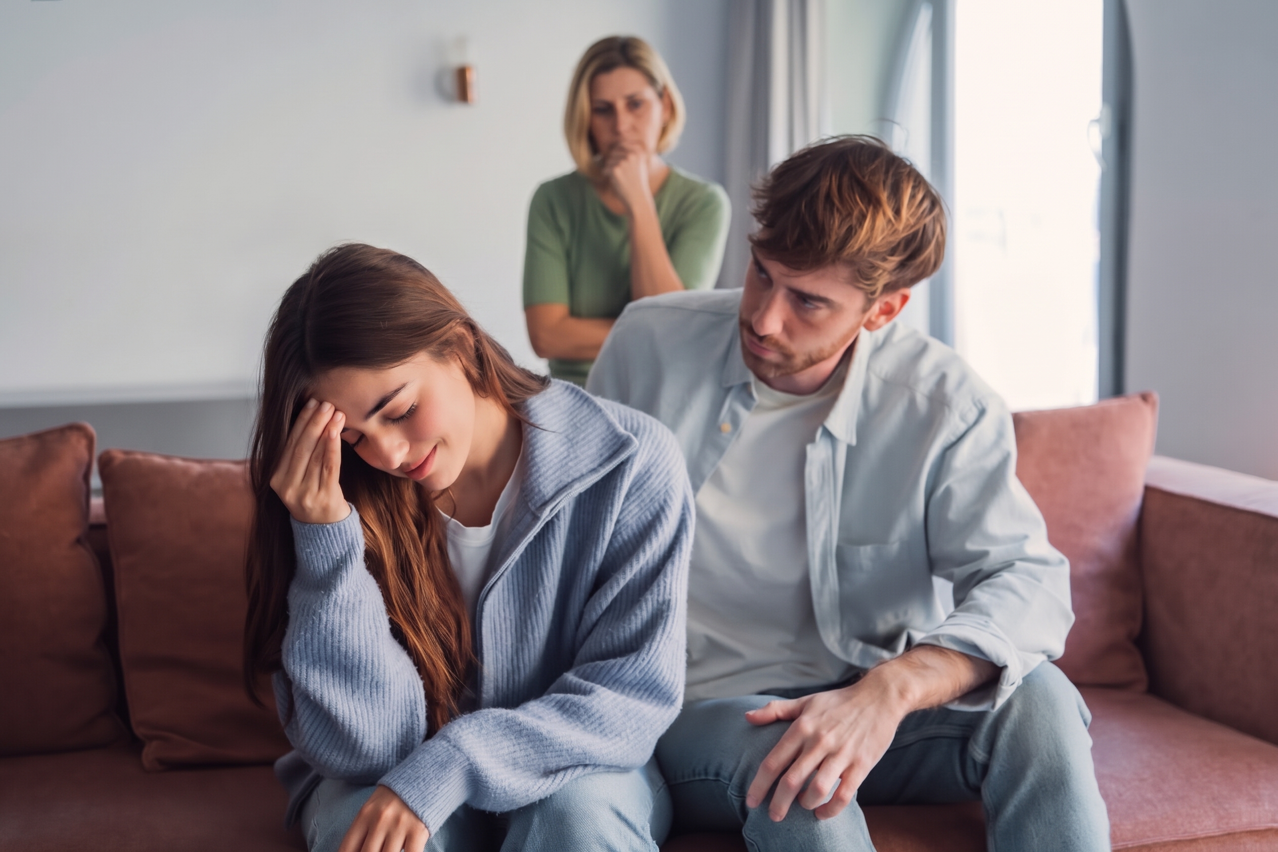 A worried man comforting his stressed wife on a couch with MIL standing in the background. A worried man comforting his stressed wife on a couch with MIL standing in the background.