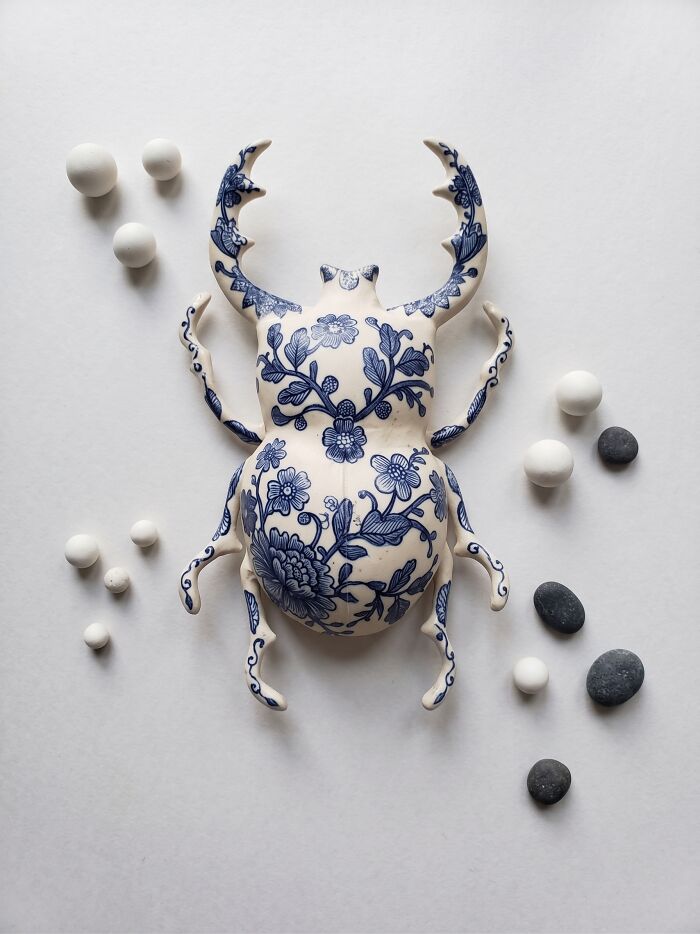 An artistic beetle sculpture with blue floral patterns, alongside small stones and spheres, reflecting childhood beliefs.