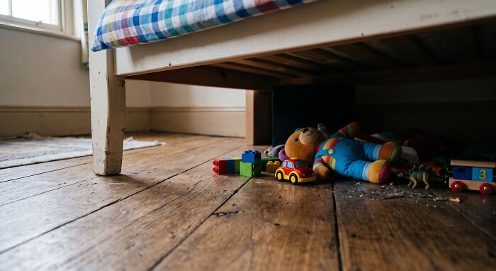 Children's toys, including a teddy bear and building blocks, are scattered under a bed, reflecting a childhood belief.