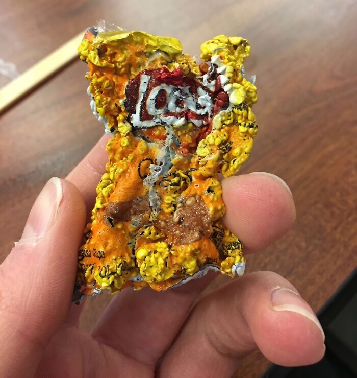 A hand holding a tiny shrunken chip bag, a cool photo of what happens if you microwave a snack wrapper.