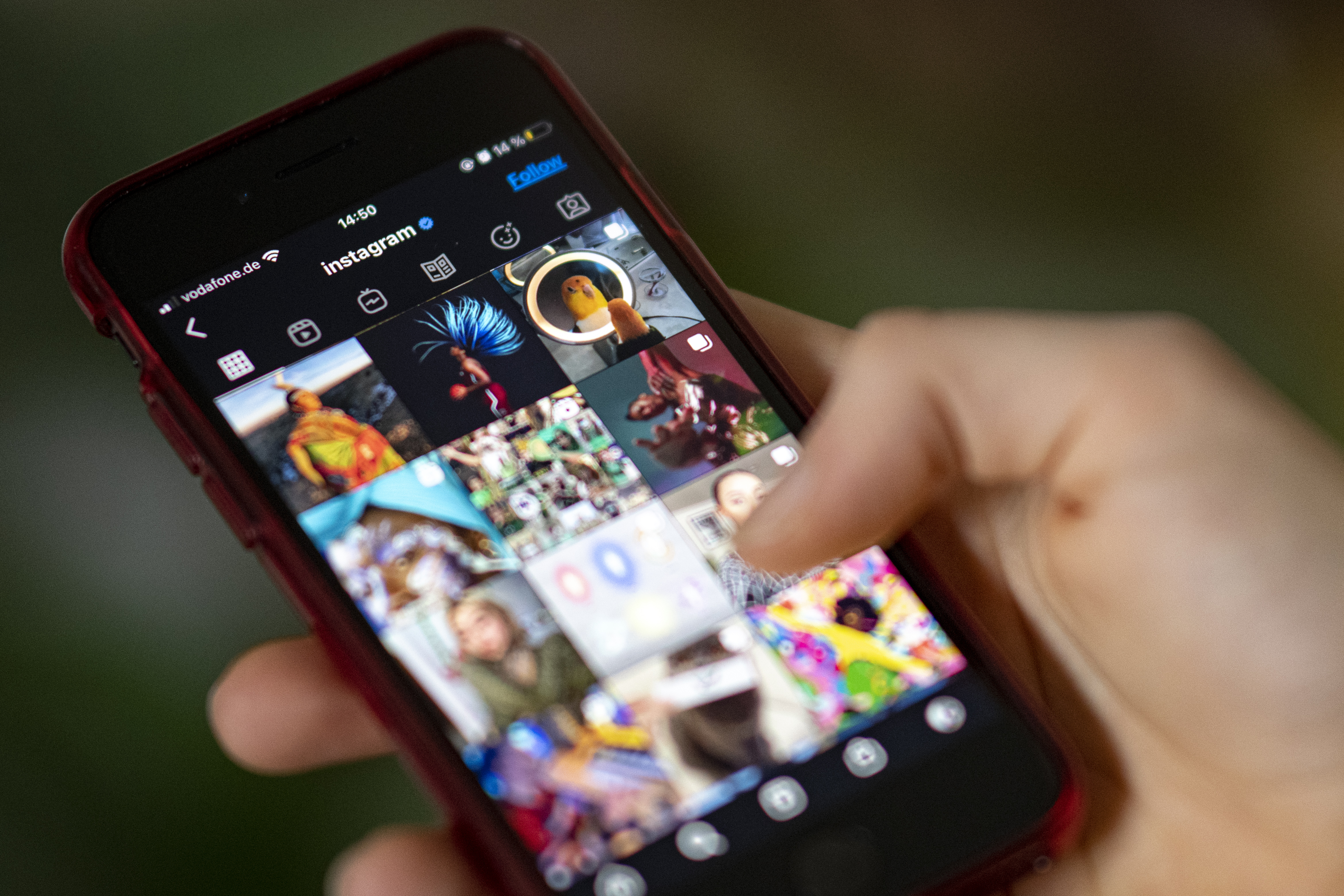 A hand holding a mobile phone showing an Instagram feed with various posts