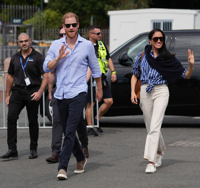Meghan Markle and Prince Harry waving, with household staff or security in the background, amidst new interview rules. Meghan Markle and Prince Harry waving, with household staff or security in the background, amidst new interview rules.