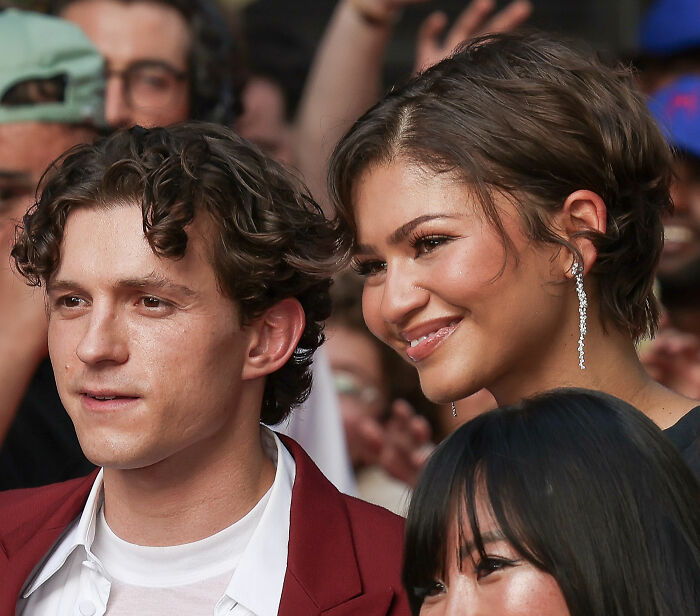 Zendaya smiles next to Tom Holland, both celebrities looking at someone off-camera. Zendaya smiles next to Tom Holland, both celebrities looking at someone off-camera.
