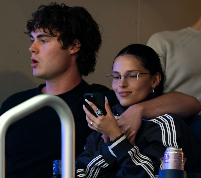 A Hollywood rising star looks at her phone while a man sits beside her, capturing the reality of fame and public scrutiny. A Hollywood rising star looks at her phone while a man sits beside her, capturing the reality of fame and public scrutiny.