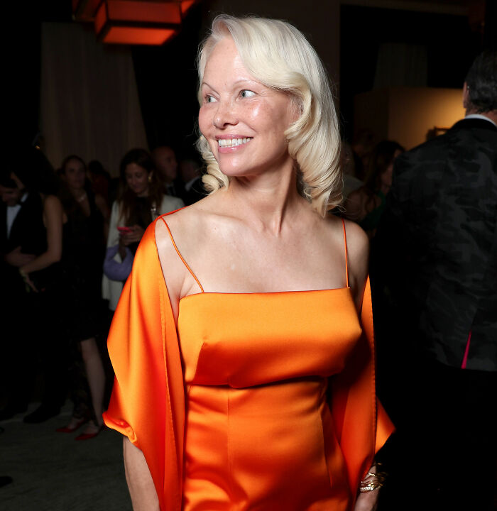 A woman with blonde hair in an orange dress, details her harrowing health battle like Pamela Anderson. A woman with blonde hair in an orange dress, details her harrowing health battle like Pamela Anderson.